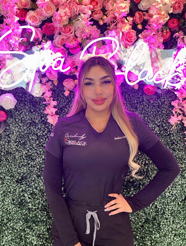 Andrea Cardenas, MA, Injector, in front of the Spa Black neon sign