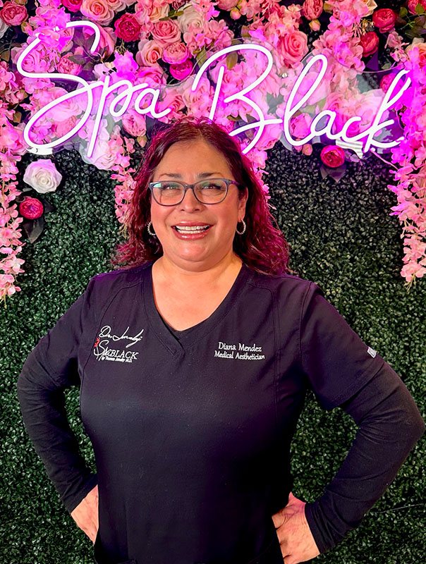 Diana Mendez, L.M.E., Licensed Esthetician, Laser & Body Sculpting Specialist, in front of the Spa Black neon sign