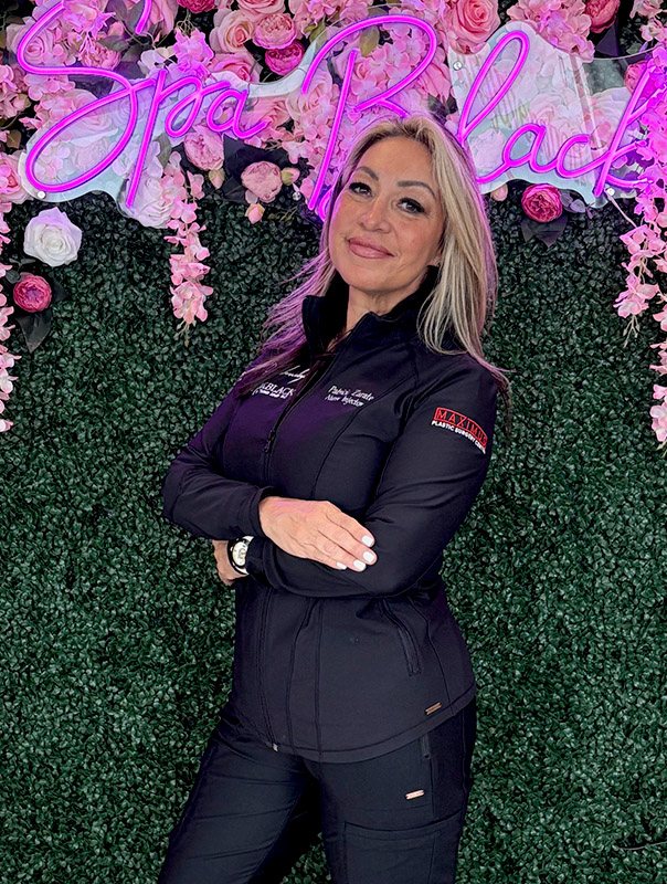 Patricia Zarate, Nurse Injector, LME, LMT, in front of the Spa Black neon sign